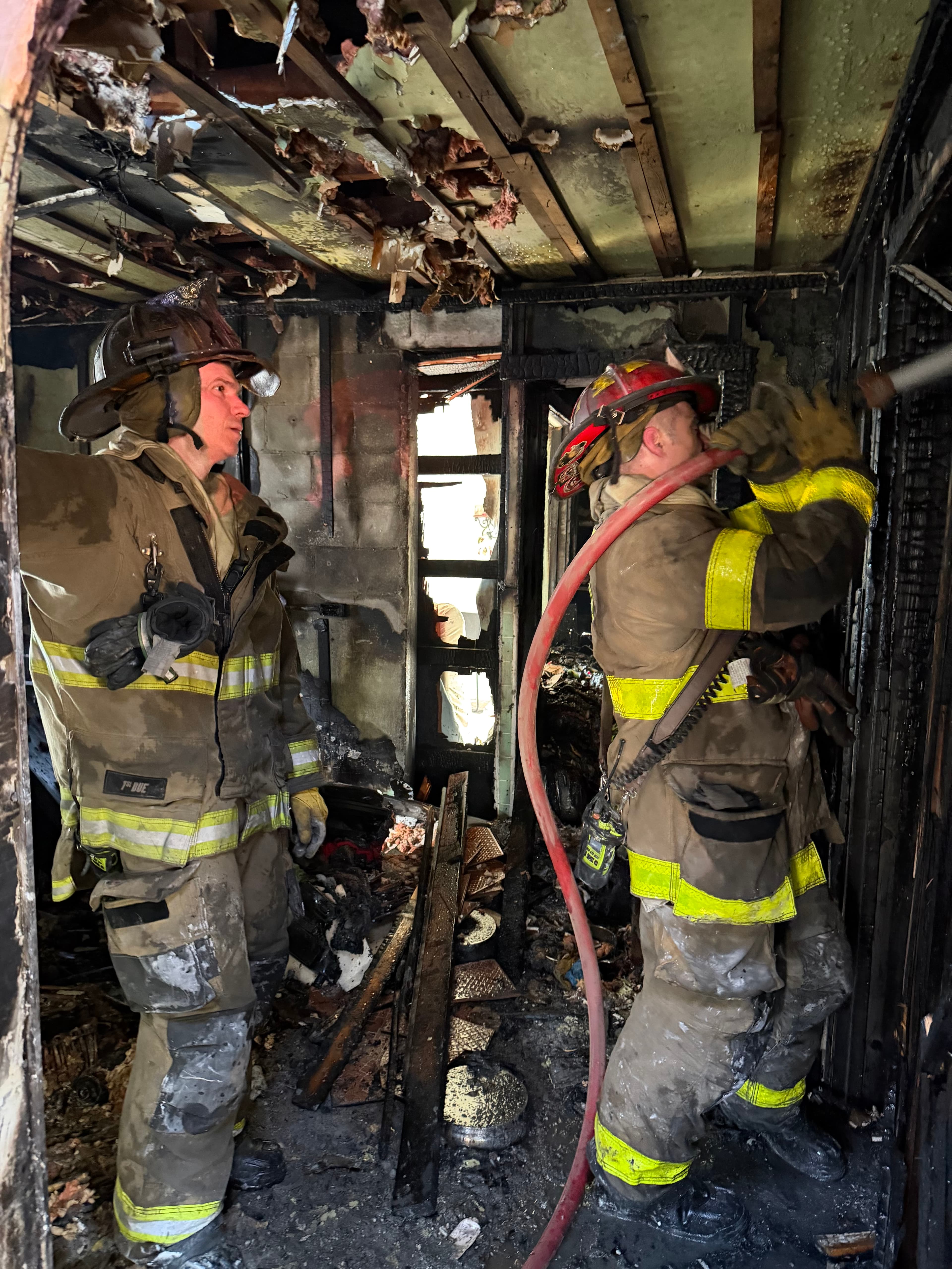 Firefighters working a hose line inside a heavily damaged burned structure at an interior fire attack
